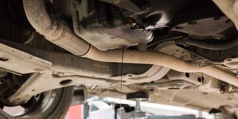 Dark fluid leaks from an engine oil pan near exhaust pipes, illustrating maintenance issues that can impact engine performance.