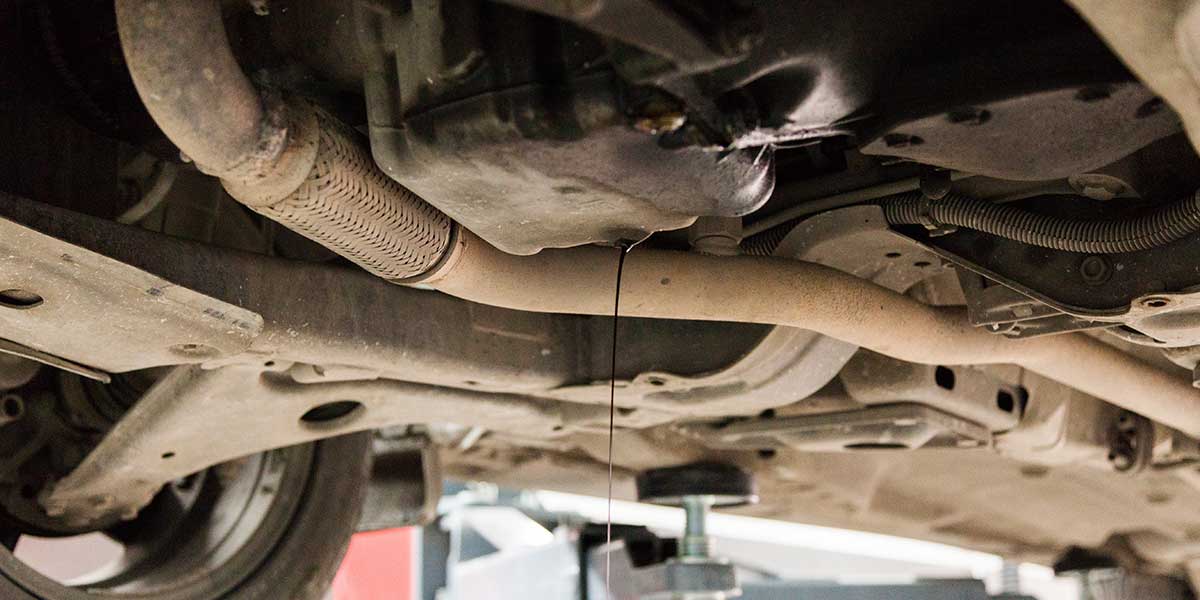Dark fluid leaks from an engine oil pan near exhaust pipes, illustrating maintenance issues that can impact engine performance.